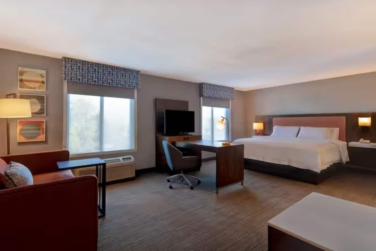 A hotel room with a bed, desk, chair, and a TV.