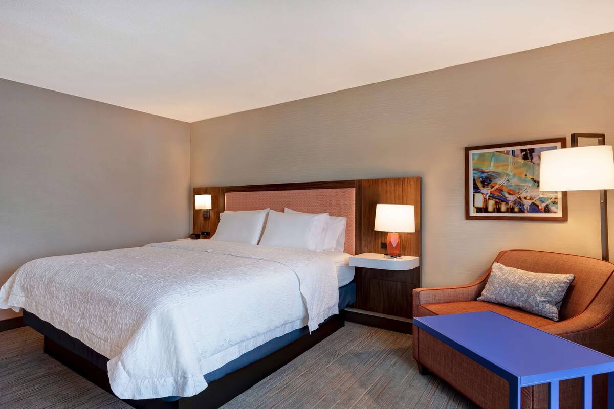 A hotel room with a large bed, a nightstand with a lamp, a sofa, and a painting on the wall.