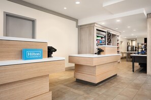 A hotel reception area with wooden reception desks, a blue sign reading 'Hilton Honors,' and a well-lit interior. - Hilton Garden Inn Fort Collins (Fort Collins)