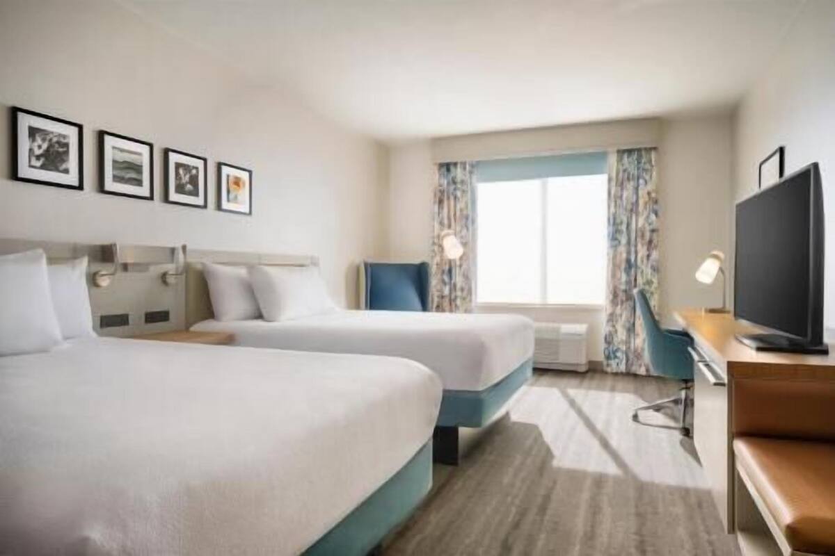 A hotel room with two beds, a desk with a chair, a television, and a window with curtains.