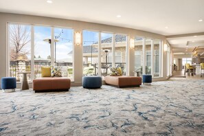 A spacious lobby with large windows, a patterned carpet, and a seating area with ottomans. - Hilton Garden Inn Fort Collins (Fort Collins)