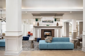 A spacious lobby with a fireplace, a blue sofa, and a high ceiling. - Hilton Garden Inn Fort Collins (Fort Collins)