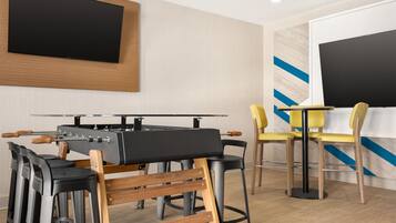A modern bar area with a foosball table, bar stools, and a TV mounted on the wall.