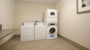 Una sala de bugaderia amb dues piles de rentadores i assecadores, una taulella i un quadre penjat a la paret.