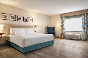 A hotel room with a bed, a chair, a lamp, a window with curtains, and a wall with framed pictures. - Hilton Garden Inn Fort Collins (Fort Collins)