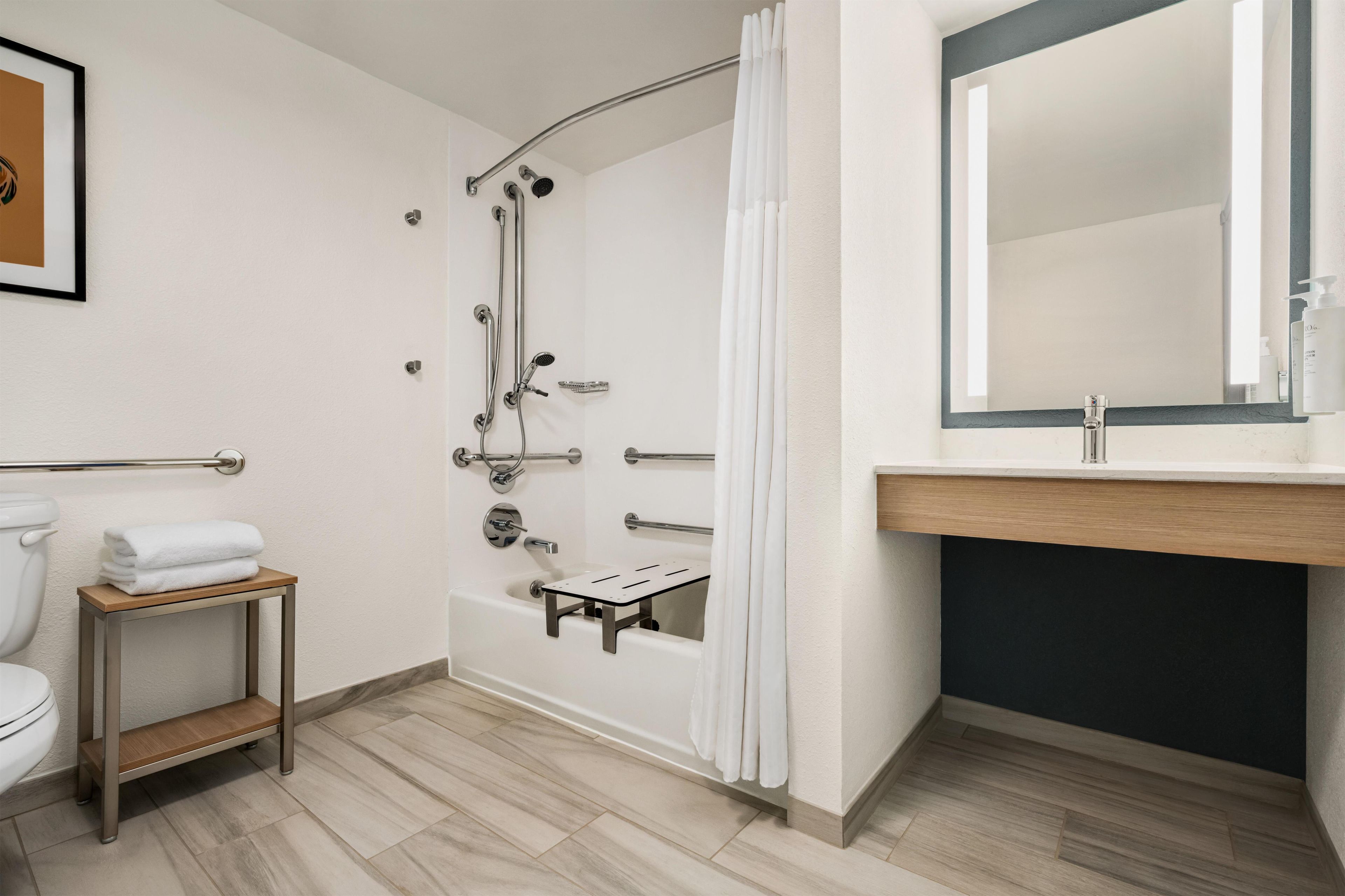 A modern bathroom with a bathtub, shower, toilet, and a small table with towels.