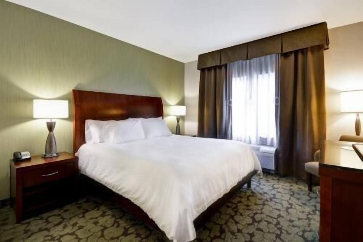 A hotel room with a large bed, two bedside lamps, a nightstand, and a window with curtains.