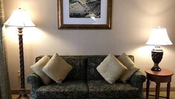 A living room with a dark green patterned sofa, two lamps, and a framed picture on the wall.