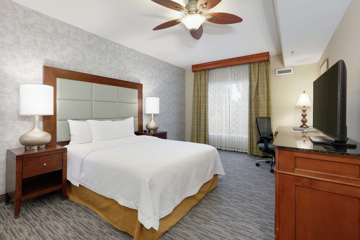 Habitación de hotel con una cama grande, dos mesitas de noche con lámparas, un televisor, un escritorio y un ventilador de techo.