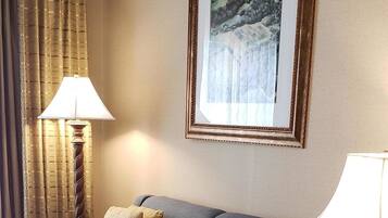 A hotel room with a grey sofa, two yellow pillows, a framed picture on the wall, and two lamps.