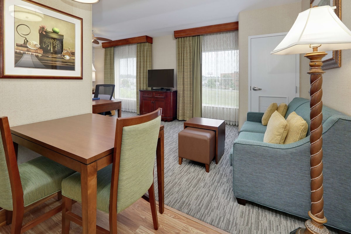 Una habitación de hotel con una mesa de comedor, sillas, un sofá, un televisor y una lámpara.