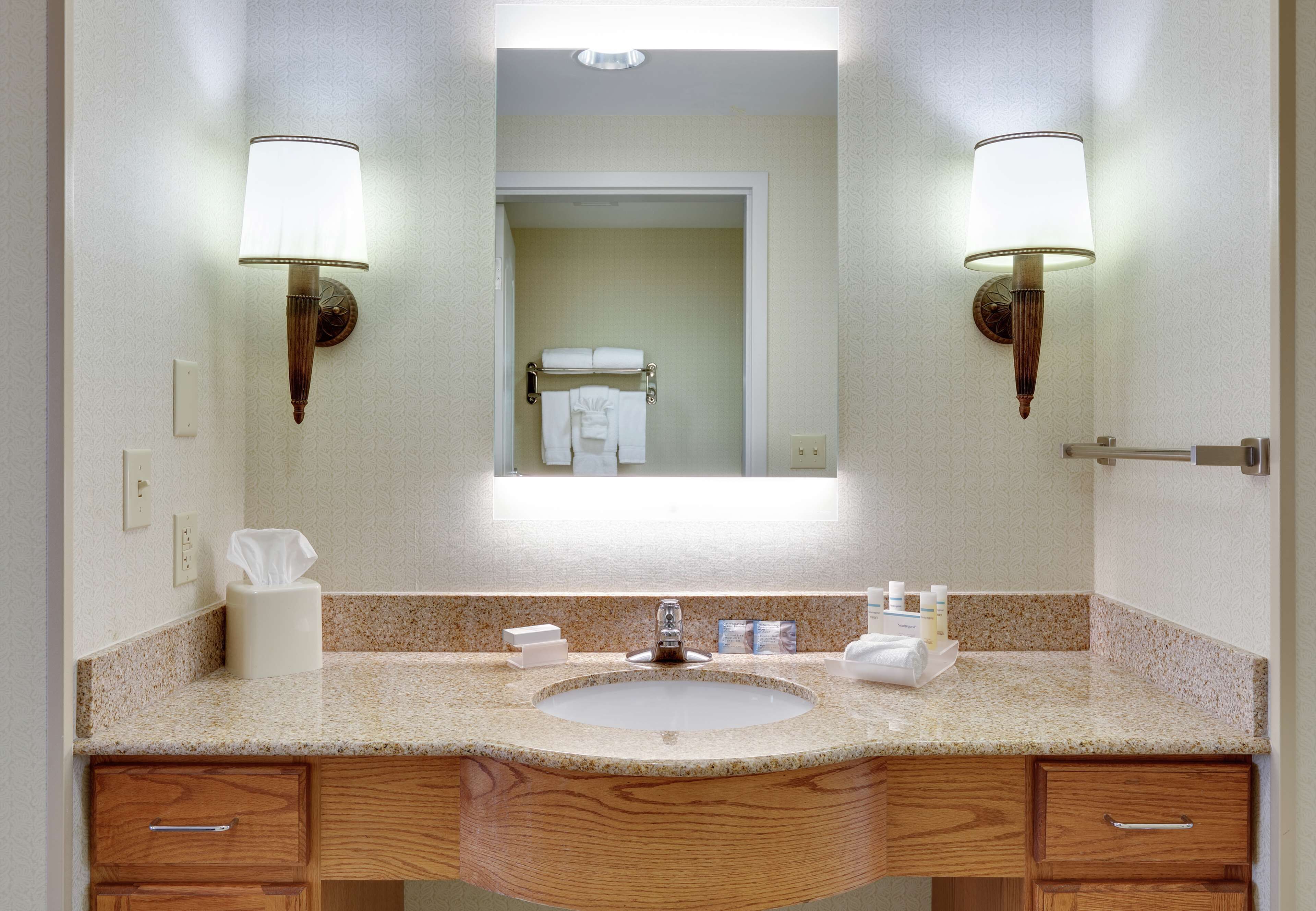 A bathroom with a sink, mirror, towel rack, and two wall-mounted lamps.