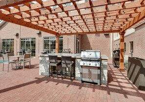 Een terras buiten met een tegelvloer, een barbecuehoek en een pergola.