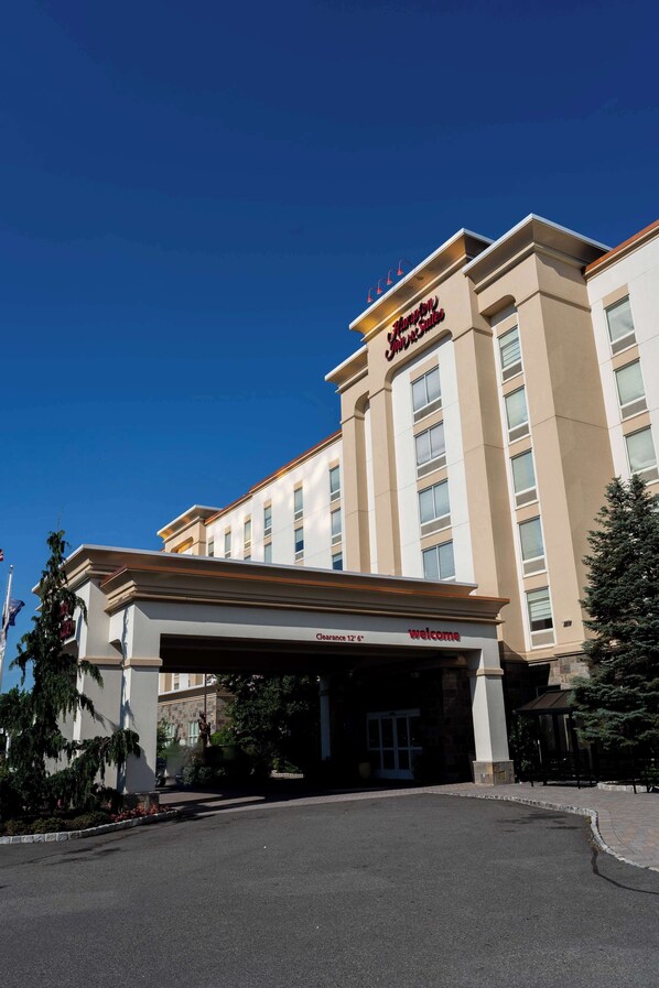 A hotel entrance with a clear sky, a welcoming sign, and a large parking area. - Hampton Inn & Suites Staten Island (Staten Island)