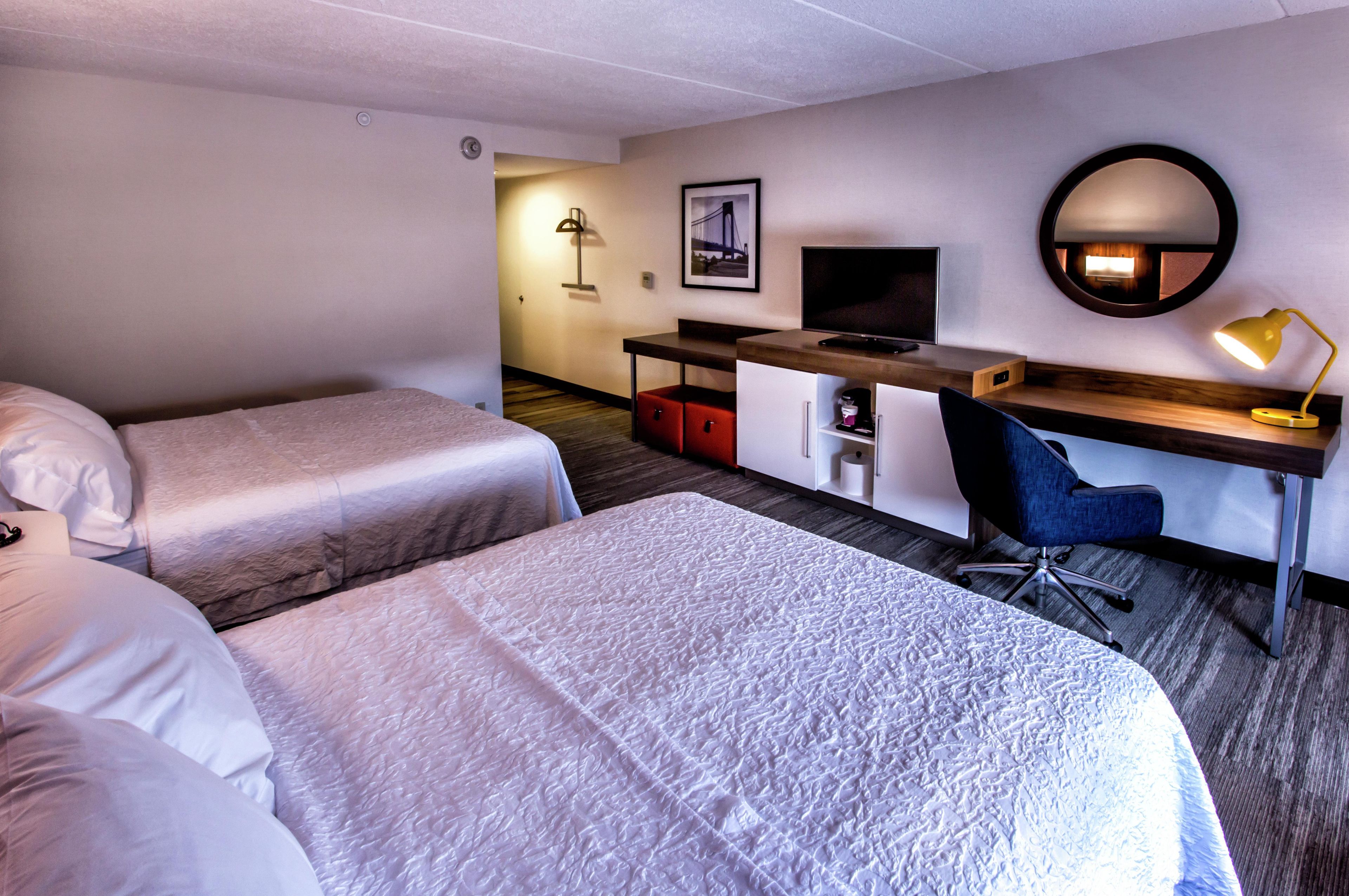 A hotel room with two beds, a desk with a computer, a chair, a desk lamp, and a framed picture on the wall.