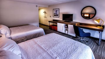 A hotel room with two beds, a desk with a computer, a chair, a desk lamp, and a framed picture on the wall.
