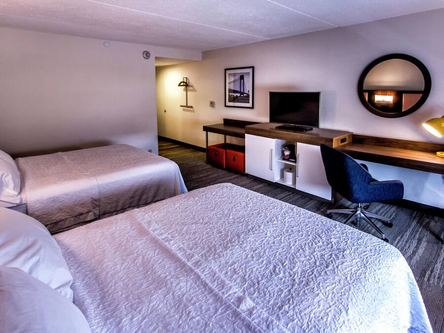 A hotel room with two beds, a desk with a computer, a chair, a desk lamp, and a framed picture on the wall.