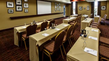 A conference room with tables set for a meeting, chairs, a projector screen, and framed pictures on the walls.