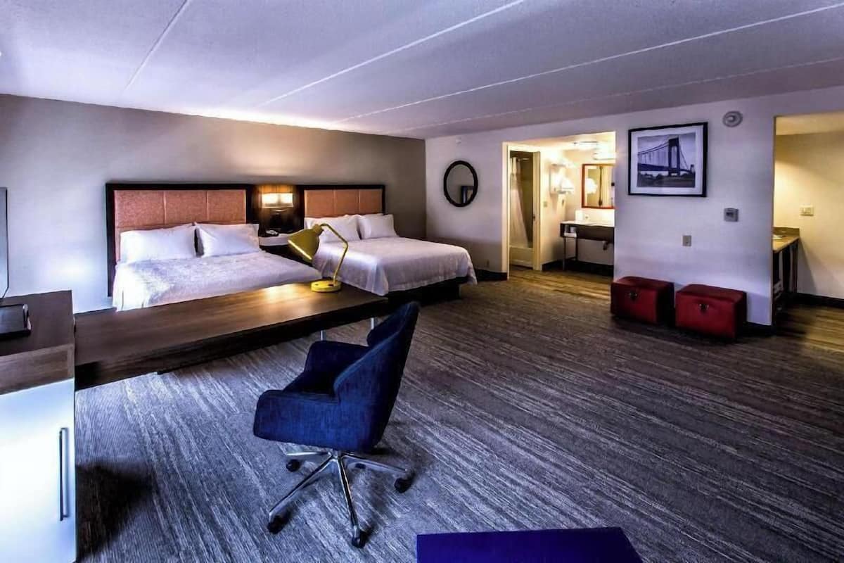 A hotel room with a bed, desk, chair, and a small kitchenette.