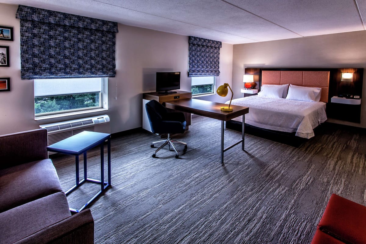 A hotel room with a bed, desk, chair, and a television.