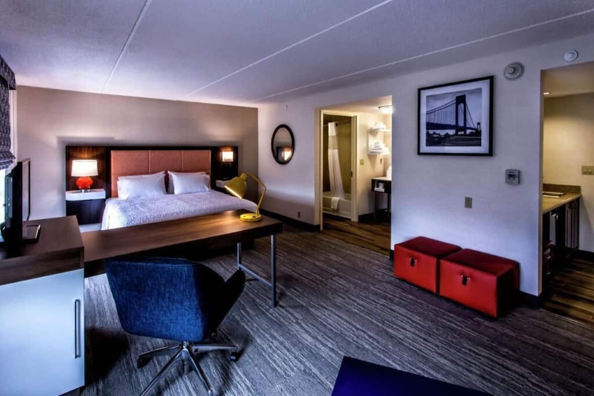 A hotel room with a bed, desk, chair, and a red storage unit.
