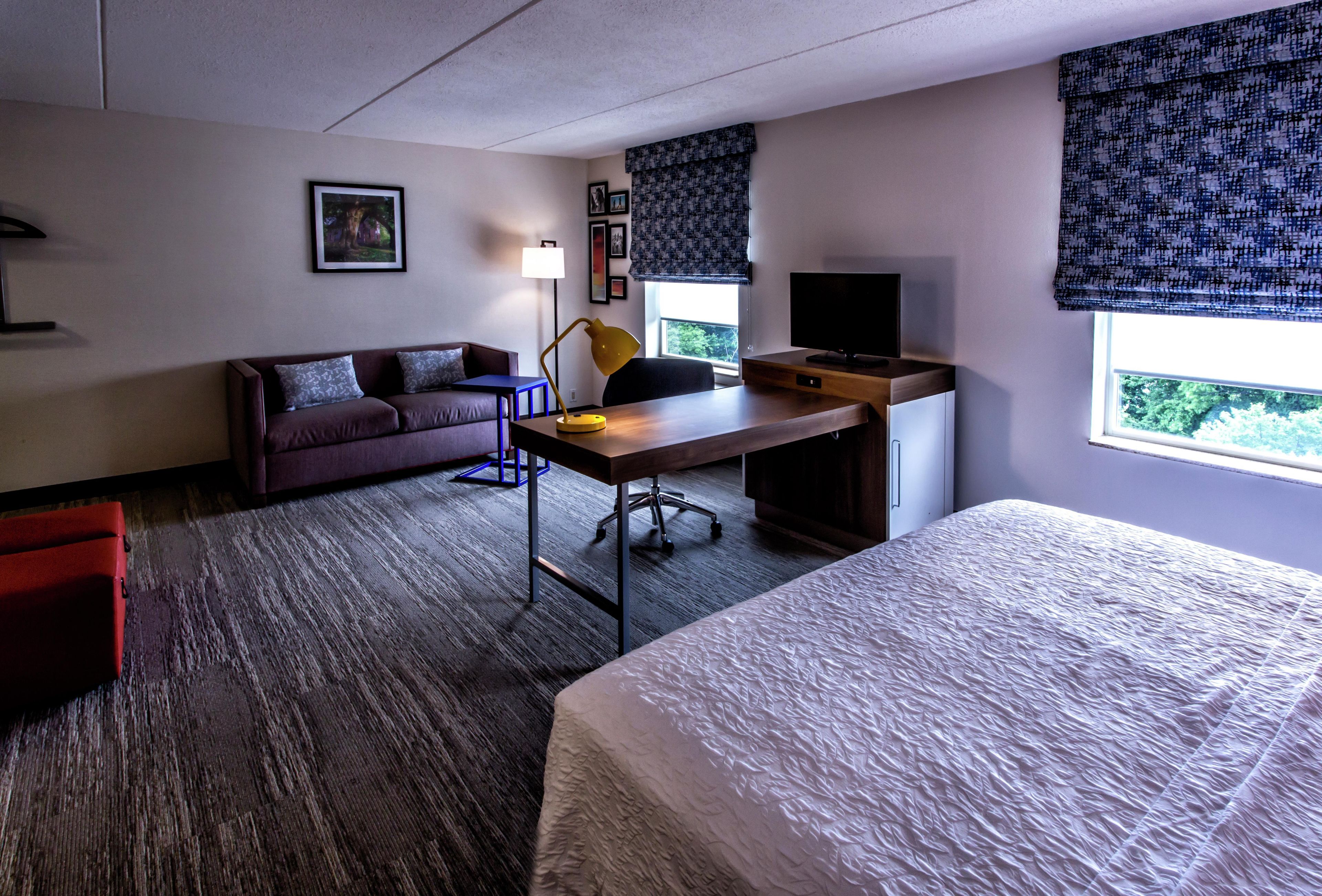 Una habitación de hotel con una cama, un escritorio con computadora, un sofá y una ventana con persianas.