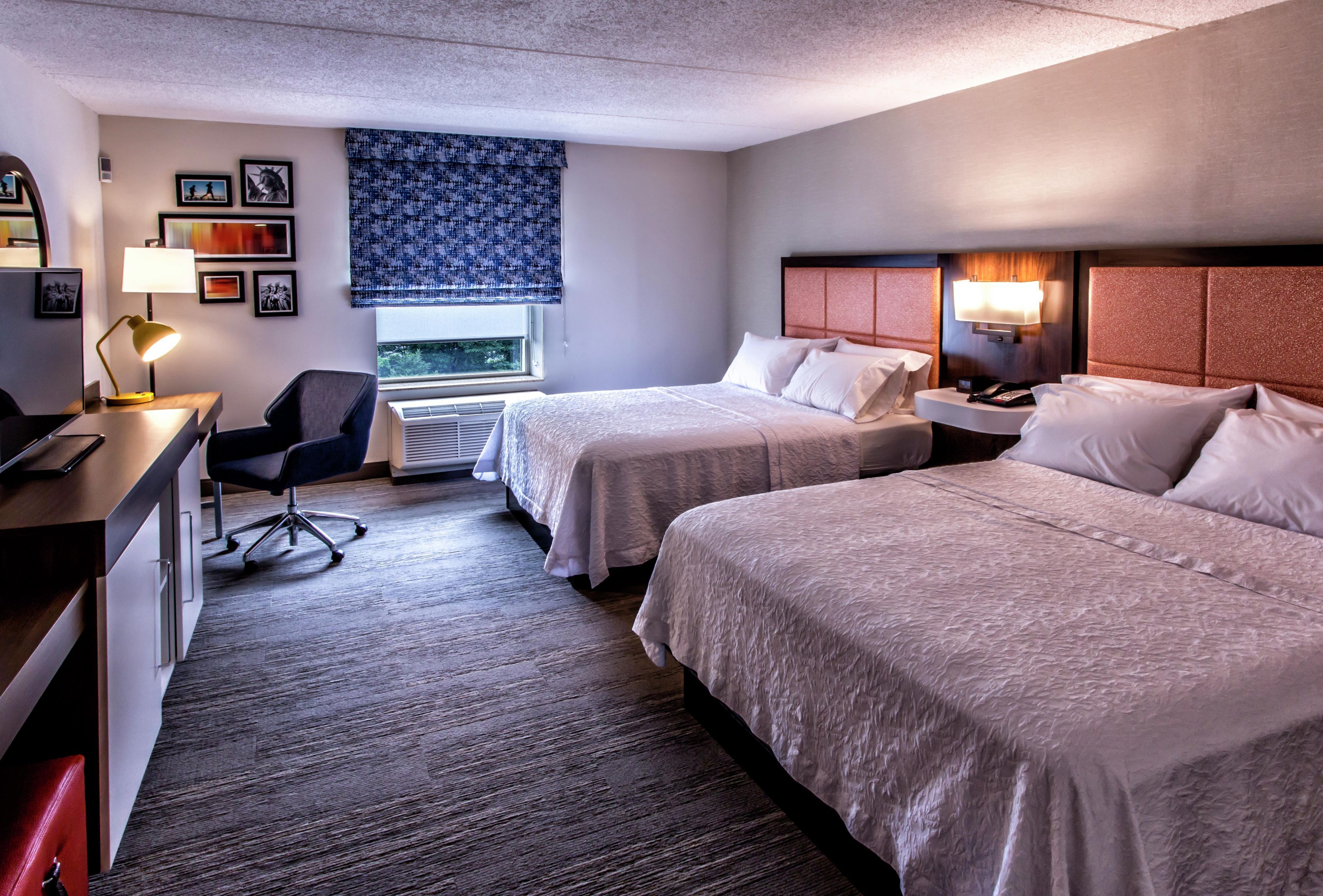 A hotel room with two beds, a desk, a chair, and a window with a view.