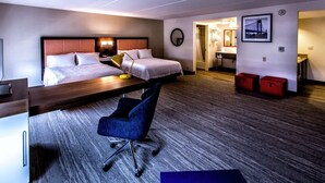 A hotel room with two beds, a desk, a chair, a desk lamp, a mirror, and a framed picture on the wall.