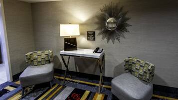 Habitación de hotel con dos sillones, un escritorio con lámpara, teléfono y espejo instalado en la pared.