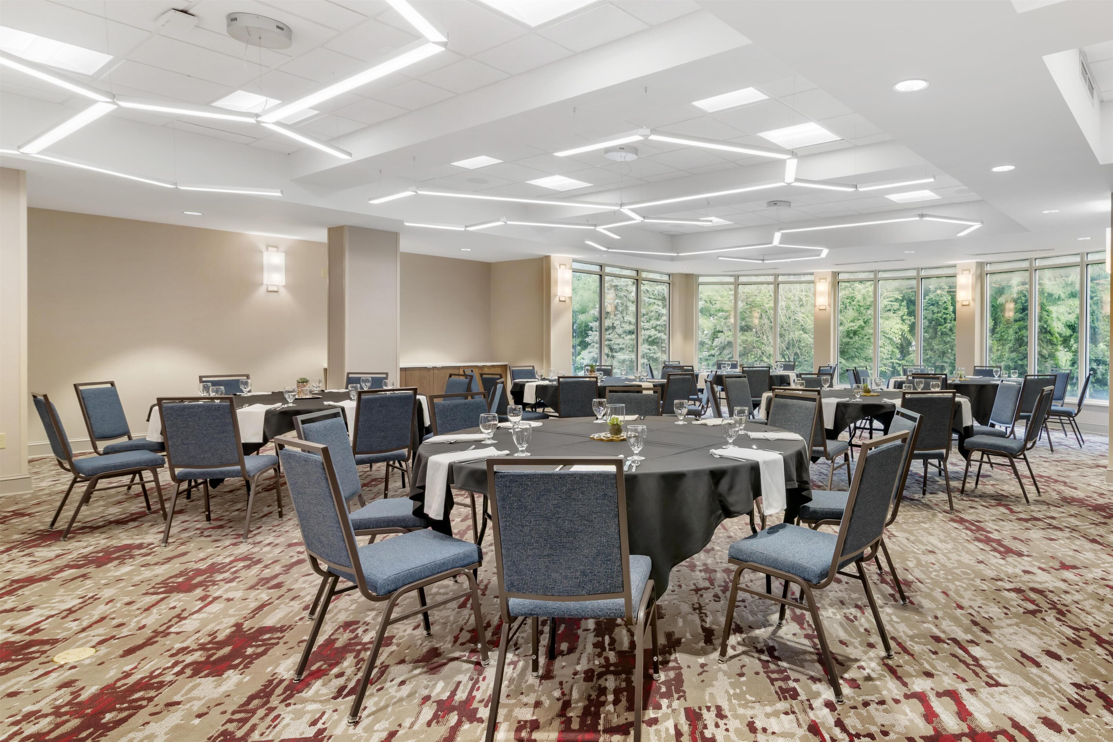 Een vergaderzaal met ronde tafels, stoelen en een vloerbedekking.