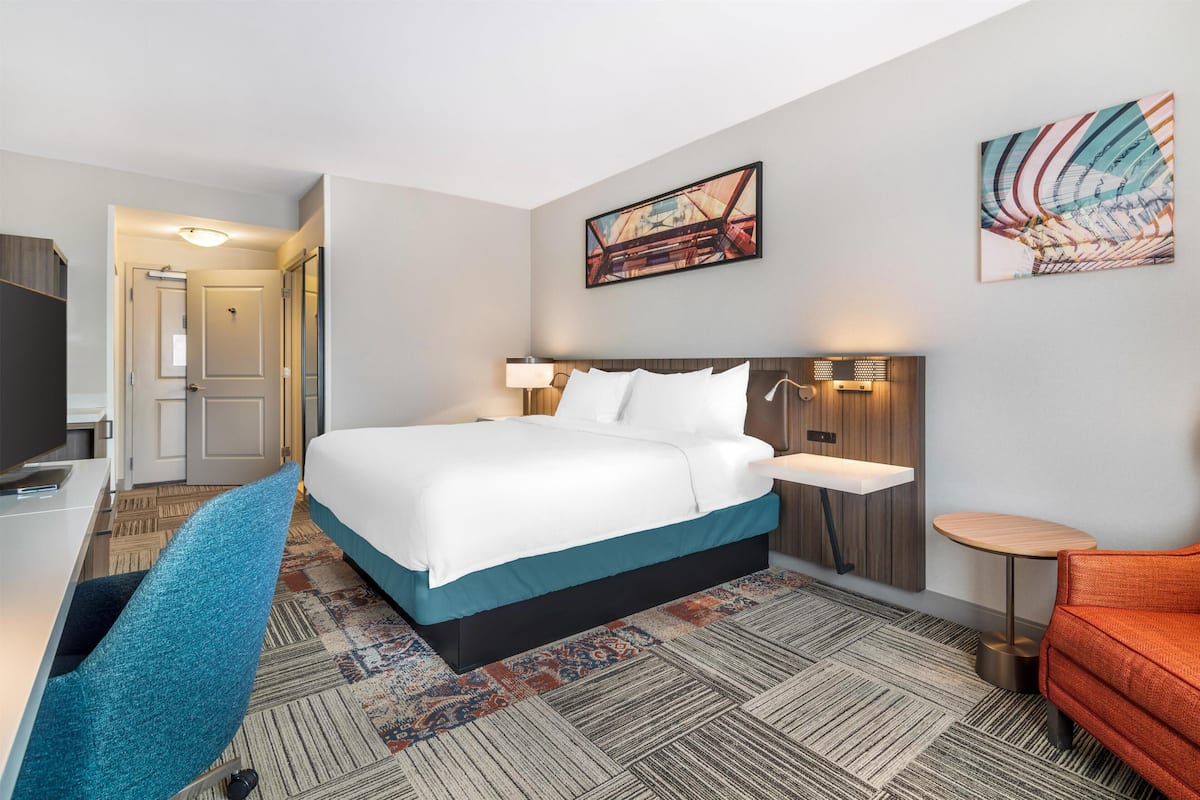 A hotel room with a bed, desk, chair, and artwork on the walls.