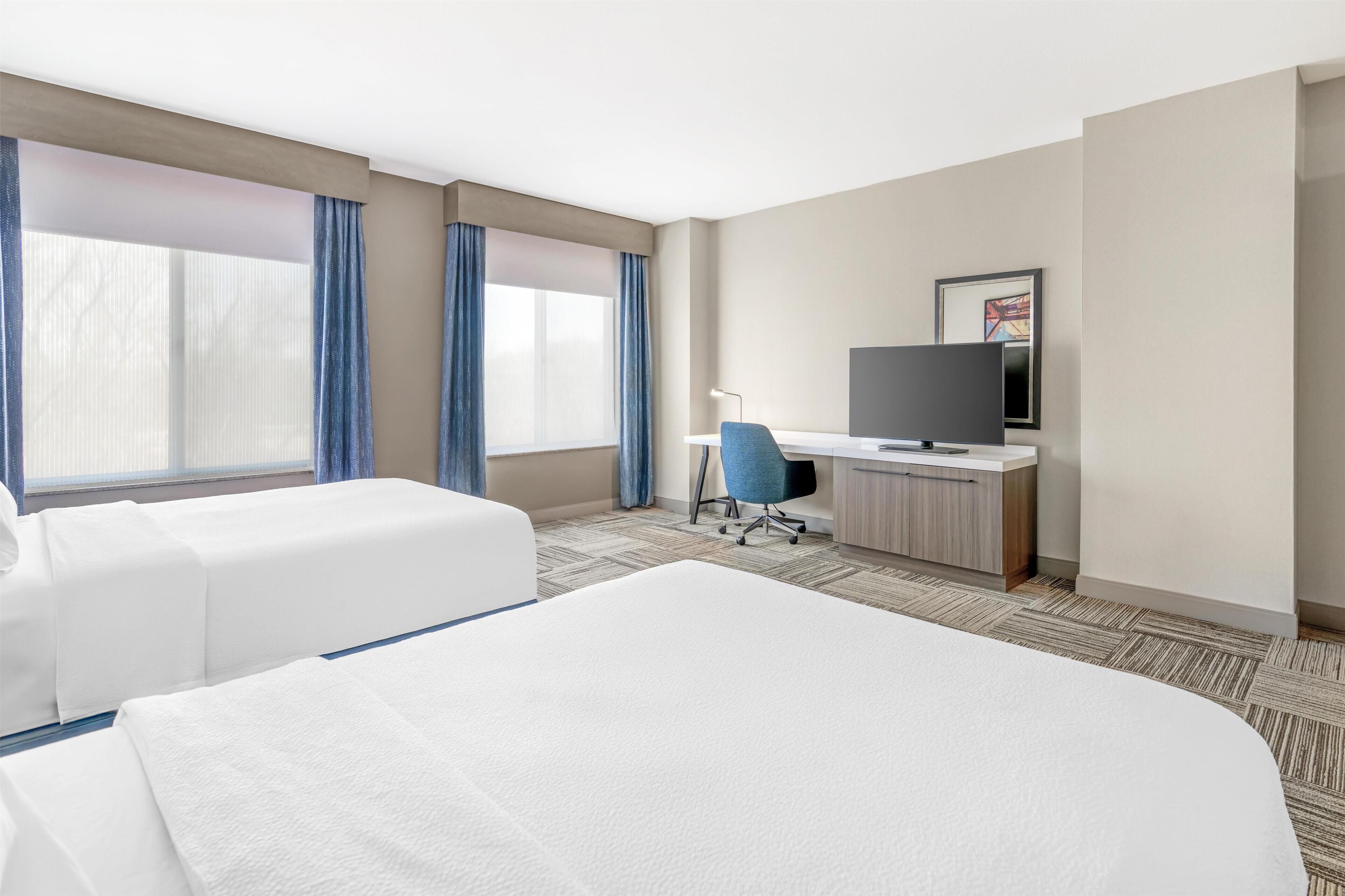A hotel room with two beds, a desk, a chair, a television, and a window with curtains.