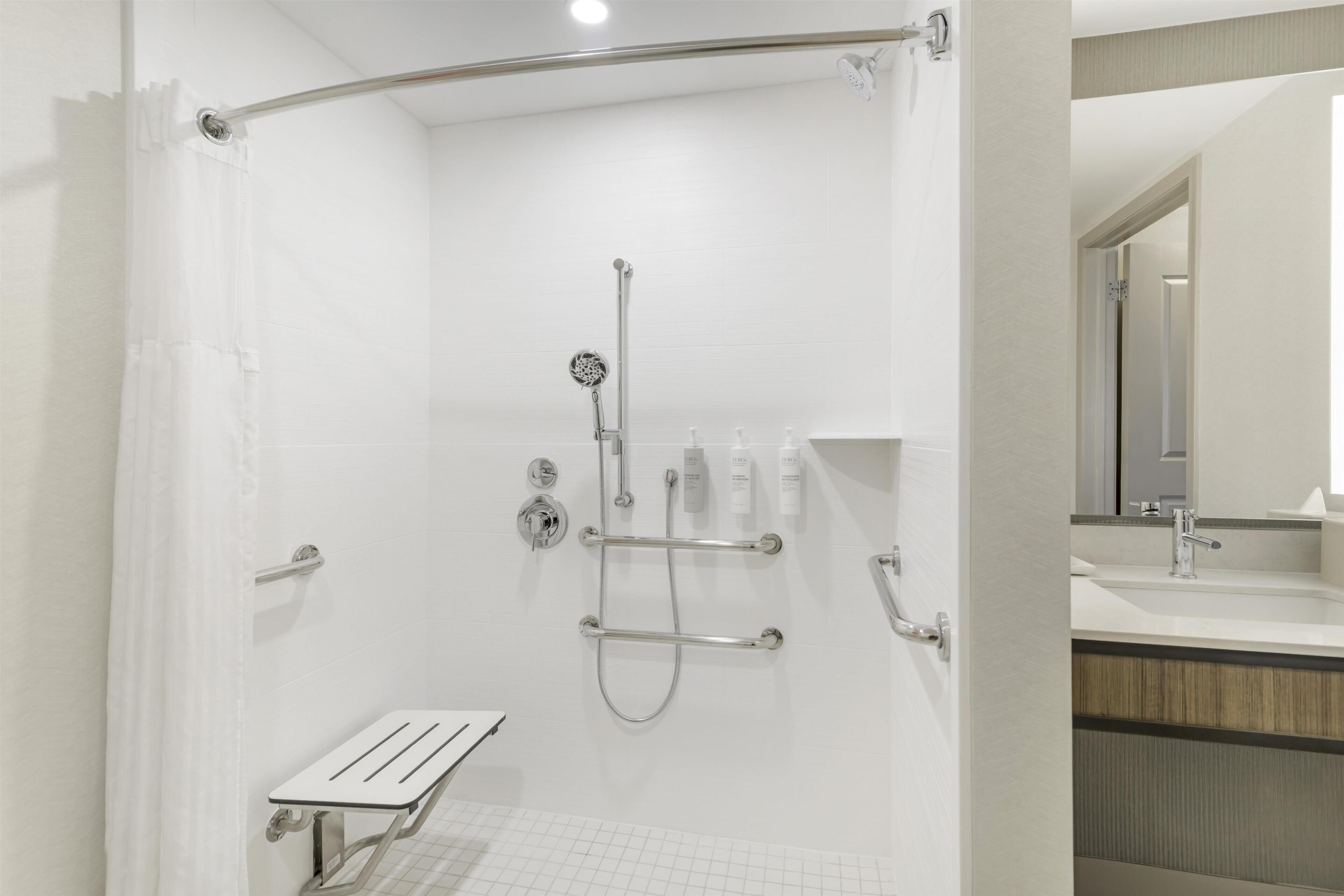 A modern bathroom with a walk-in shower, grab bars, a bench, and a vanity with a mirror.