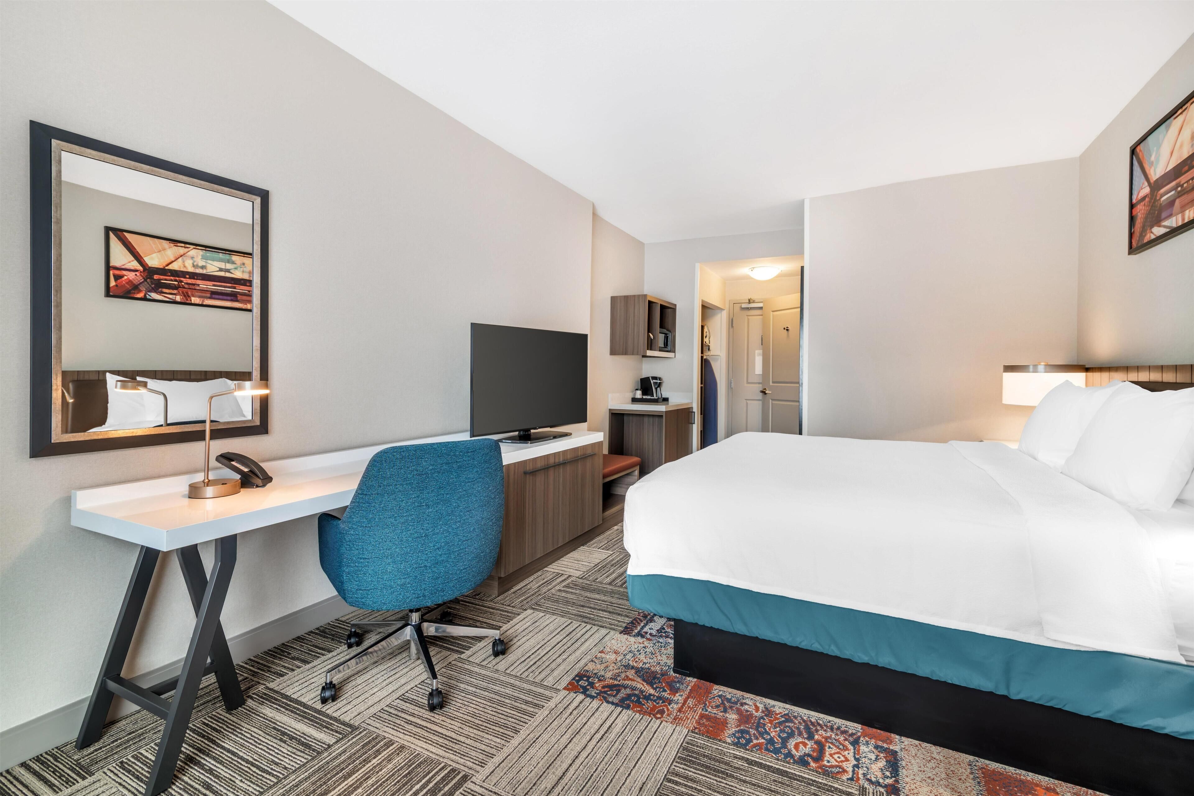 A hotel room with a bed, desk, chair, television, and a door leading to another room.