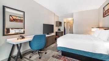 A hotel room with a bed, desk, chair, television, and a door leading to another room.