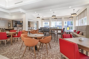 A modern hotel lobby with multiple seating areas, a kitchen, and large windows. - Hilton Garden Inn Albany/SUNY Area (Albany)