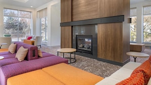 A modern living room with a fireplace, sofas, and round tables. - Hilton Garden Inn Albany/SUNY Area (Albany)