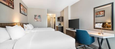 A hotel room with two beds, a desk, a chair, a TV, and artwork on the walls.