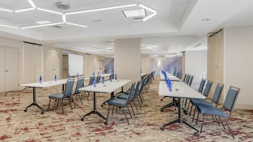 A conference room with white tables, blue chairs, and a patterned carpet.