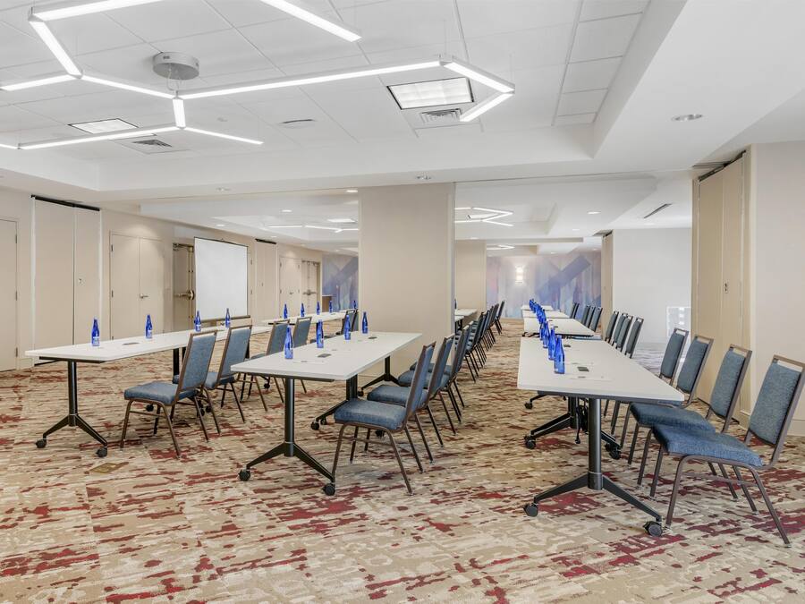 A conference room with white tables, blue chairs, and a patterned carpet.