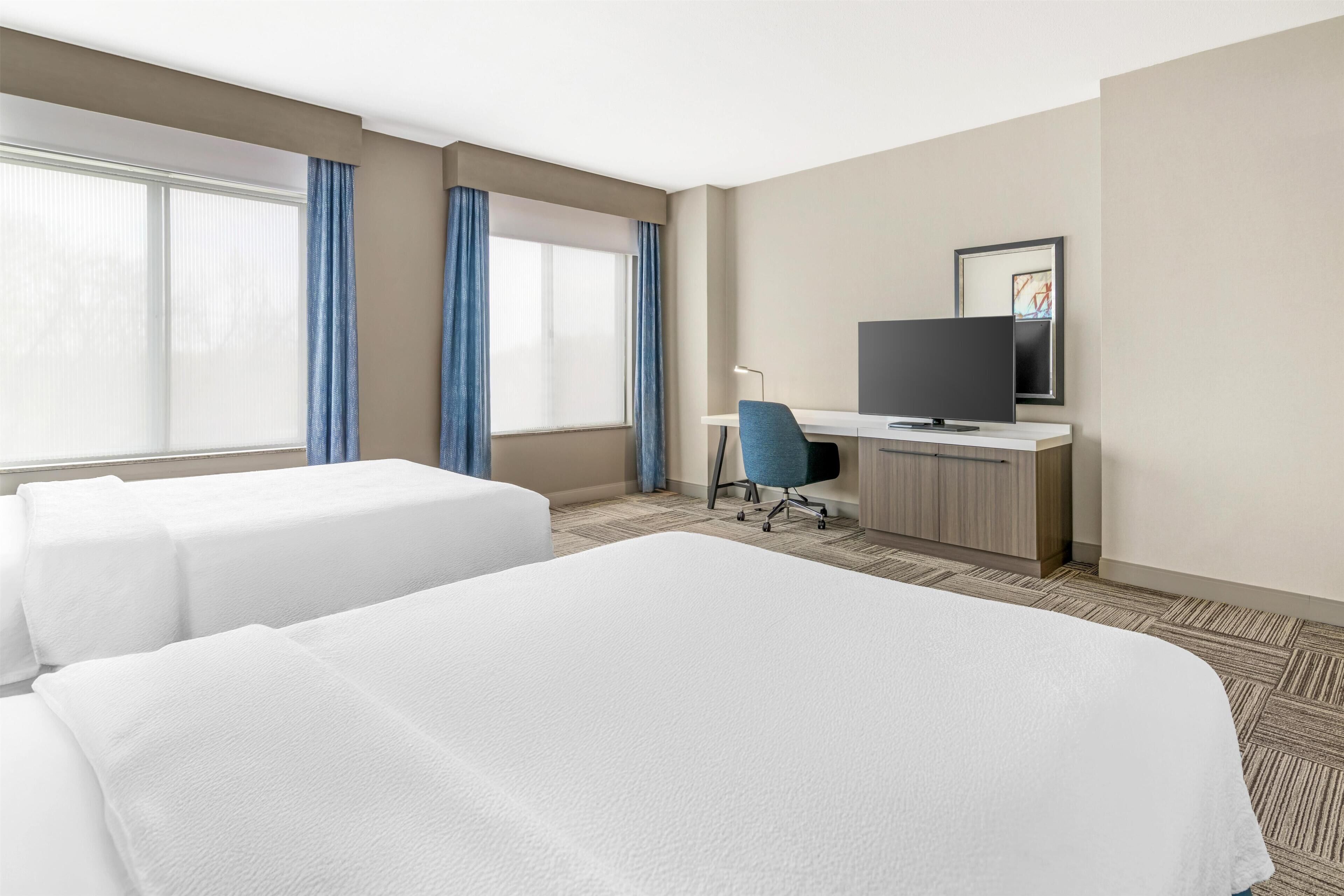 A hotel room with two beds, a desk with a TV, and a chair.