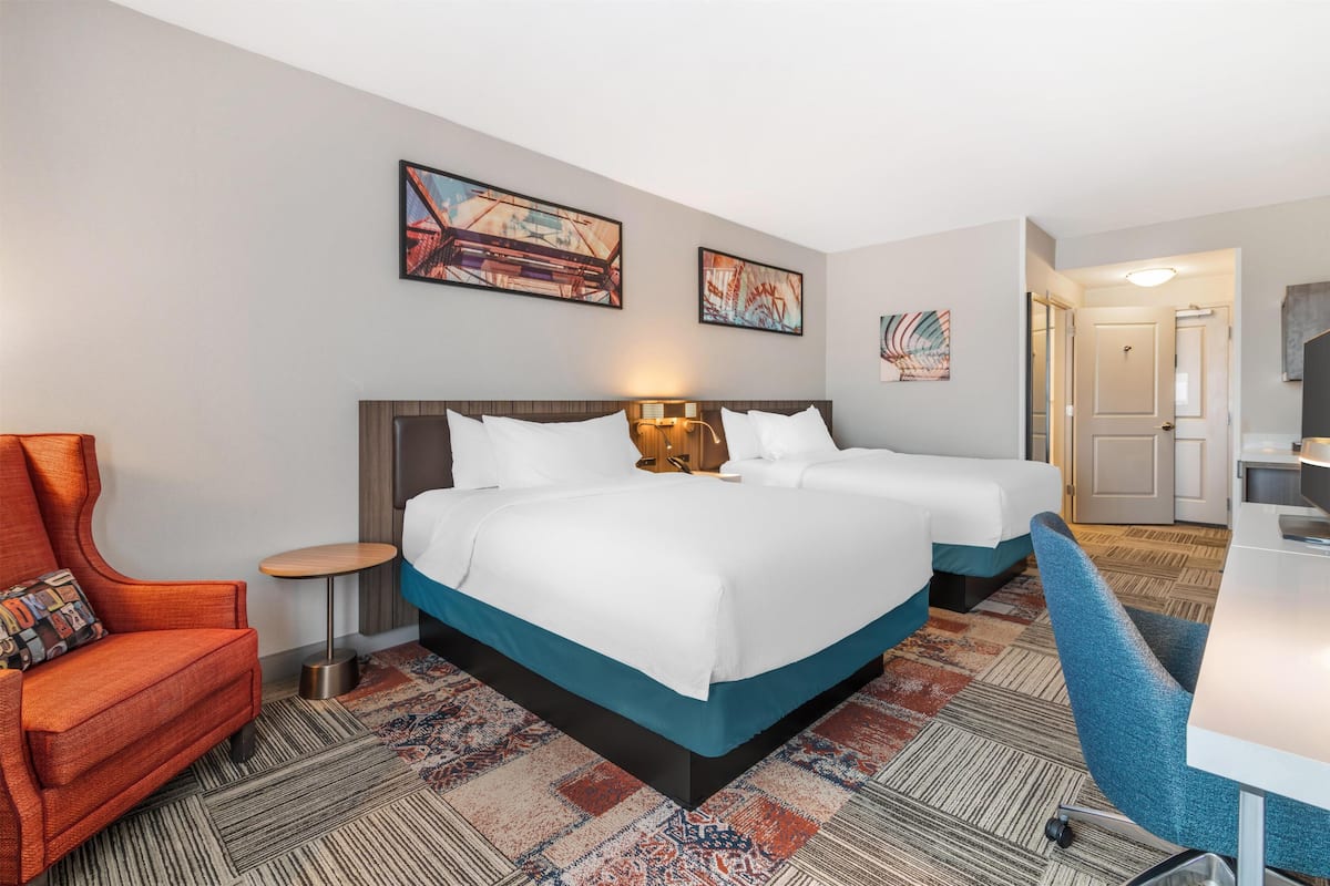 A hotel room with two beds, a desk, a chair, and artwork on the walls.