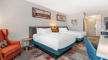 A hotel room with two beds, a desk, a chair, and artwork on the walls.
