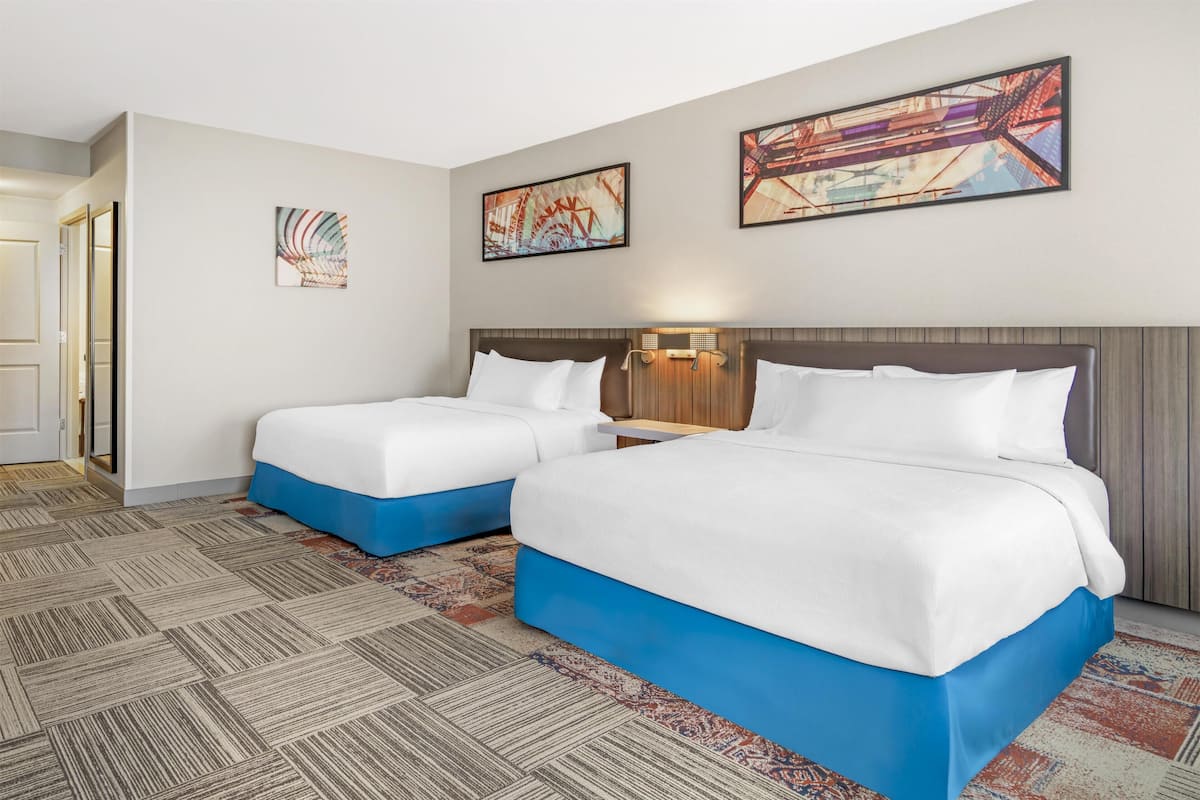 A hotel room with two beds, a patterned carpet, and three framed artworks on the wall.