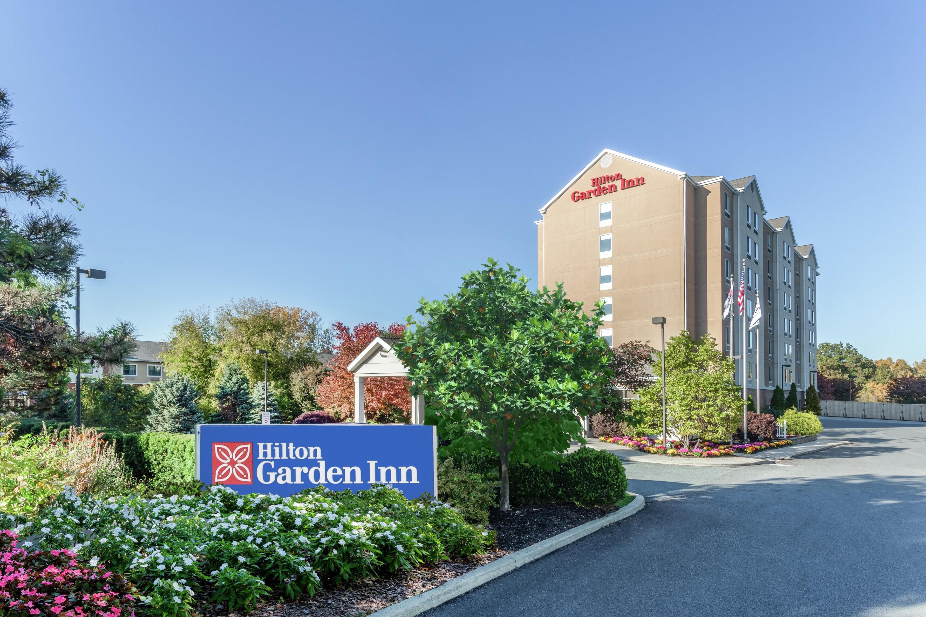 Un Hilton Garden Inn con un letrero, un estacionamiento y un edificio de fachada color crema.
