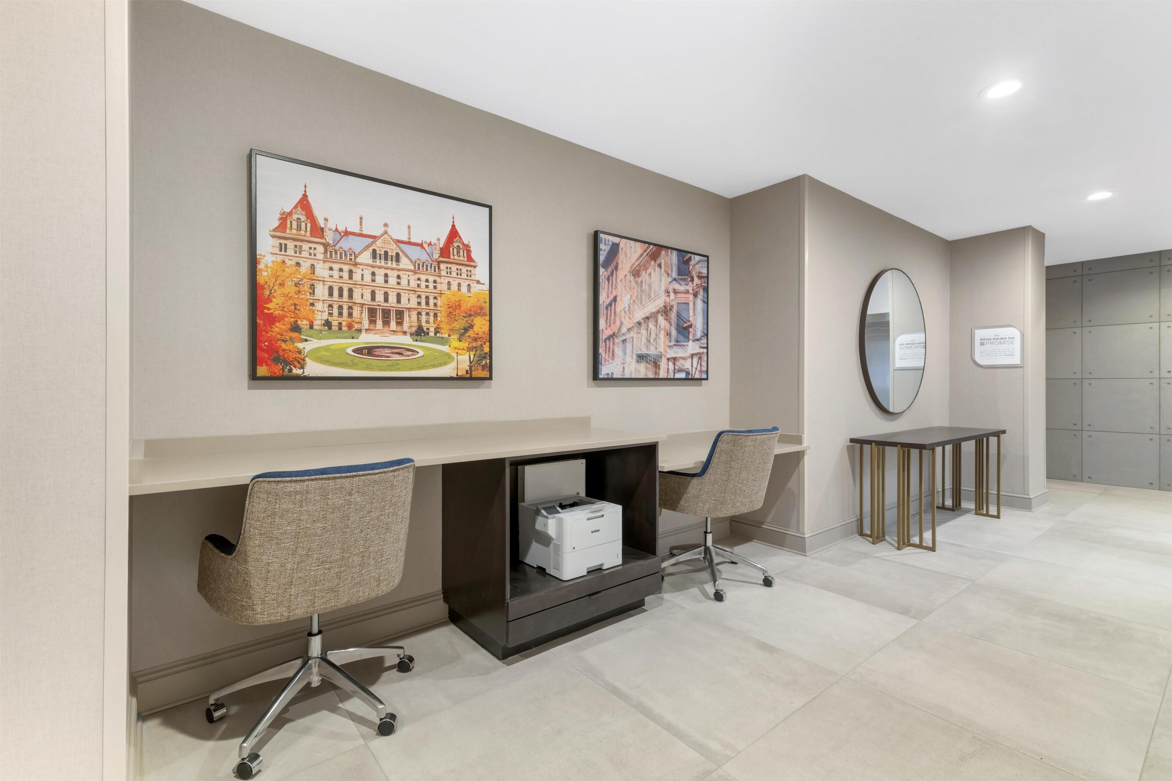 A hotel lobby with a reception desk, two chairs, a printer, and two framed pictures on the wall.