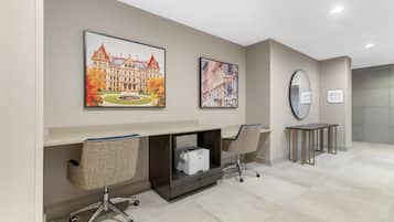 A hotel lobby with a reception desk, two chairs, a printer, and two framed pictures on the wall.