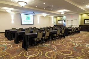 A conference room with tables and chairs, a projection screen displaying 'Holiday Inn & Suites', and an exit sign on the wall. - Holiday Inn Bloomington-Airport by IHG (Bloomington)