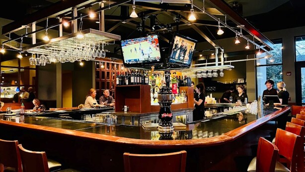 A bar area with a counter, bar stools, and a television screen displaying sports. - Holiday Inn Bloomington-Airport by IHG (Bloomington)
