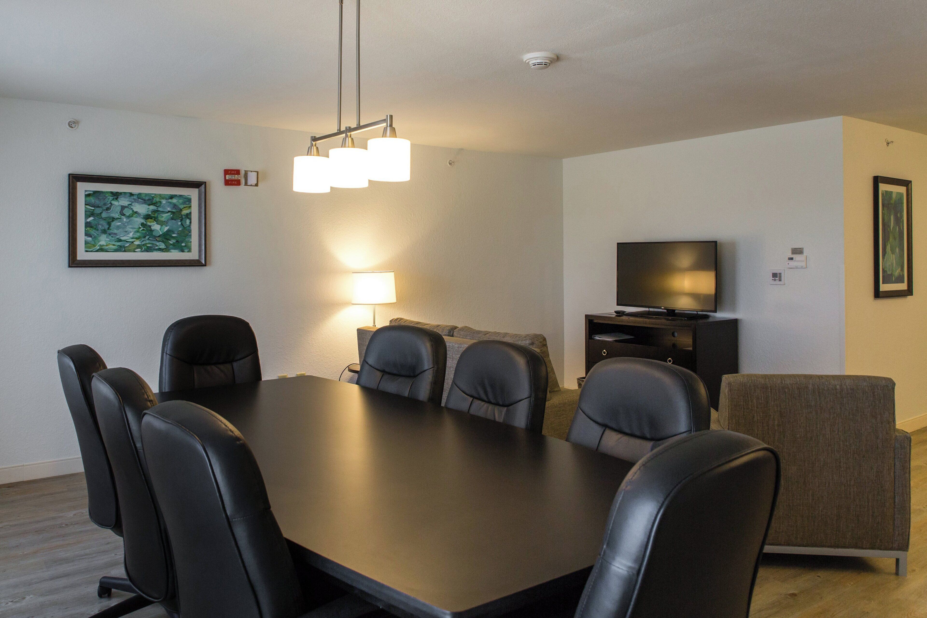 A modern living room with a dining table, chairs, a sofa, a television, and artwork on the walls.